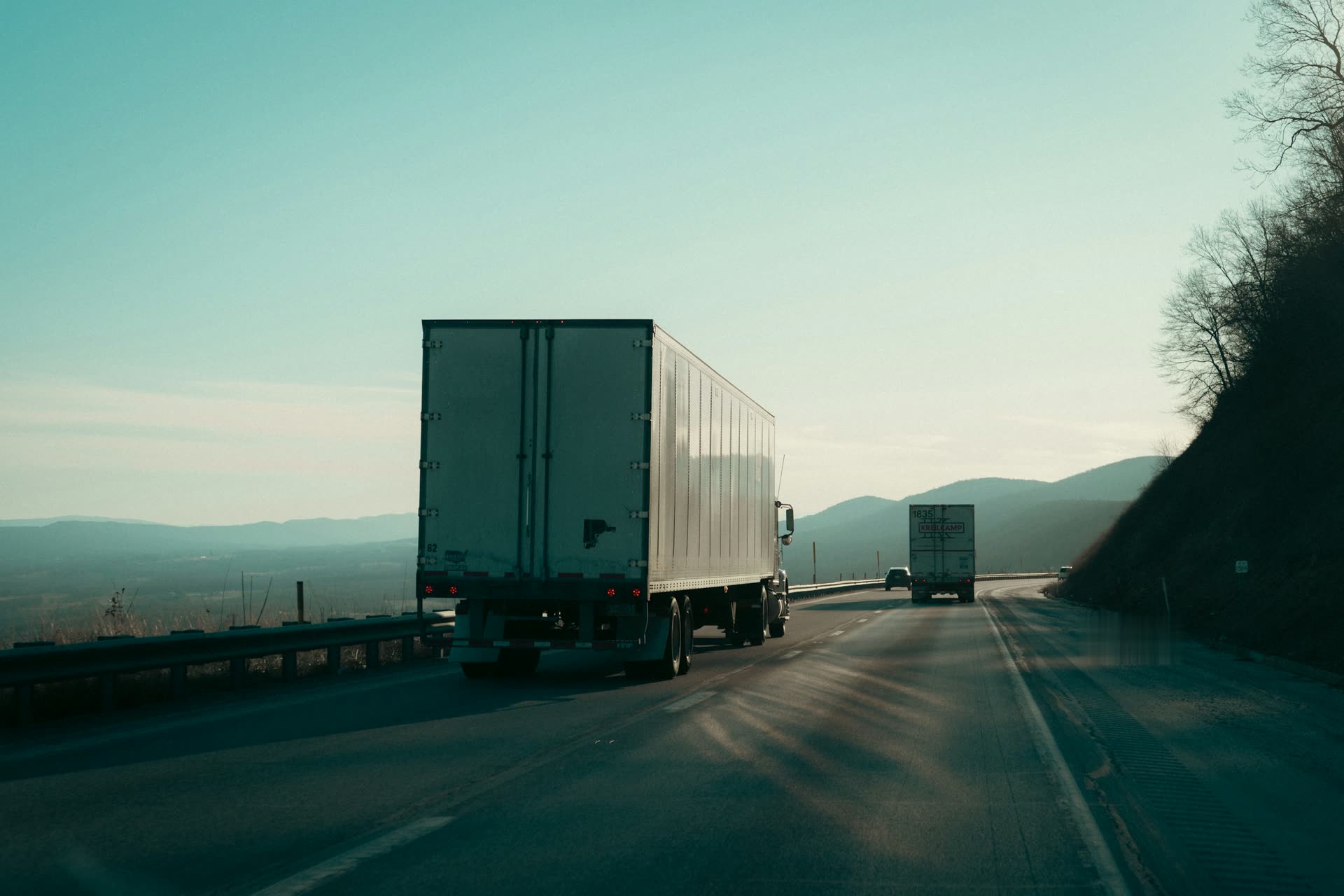 A white tractor-trailer on a mountain highway in low sun.